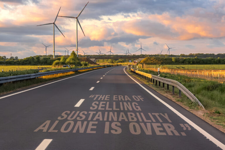 a paved two-way road with open fields on both sides and wind turbines at a distance